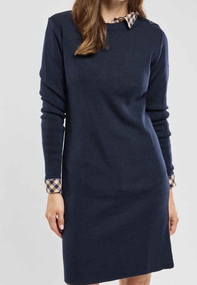 Femme portant une robe en maille bleu marine à manches longues avec col et poignets à carreaux, debout devant un fond clair uni.