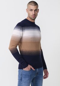 Kötött pulóver kerek nyakkal, vízszintes csíkokkal tengerészkék, bézs, világosbarna és fehér színben. Simas textura, testhezálló dizájn.