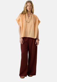 Haut pêche à manches courtes avec un décolleté en V, associé à un pantalon large bordeaux. L'ensemble est complété par un collier en perles superposé et des sandales.