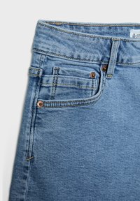 Ljusblå denimjeans med rak skärning, synliga sömmar och kopparnitar på fickorna. Har en liten framficka och en texturerad tyg.