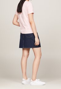 Camiseta de algodón rosa claro combinada con una minifalda de mezclilla oscura. El conjunto se complementa con zapatillas blancas. Diseño sencillo y casual.