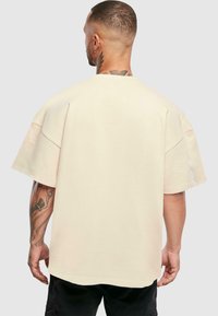 Bežinė per didelė t-shirt marškiniai trumpomis rankovėmis, apvaliu kaklu ir lygiu paviršiumi. Ypatybės - nuleistos pečių linijos dizainas ir tiesi hem.
