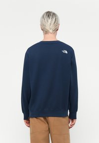 Navy blue crewneck sweatshirt with ribbed cuffs and hem. Features a white logo on the upper back. Made of soft, textured fabric.