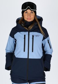 Niebieska i granatowa kurtka narciarska z kapturem, z wieloma zasuwanymi kieszeniami i czarnymi akcentami metalowymi. Gładki, wodoodporny materiał.
