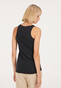 Schwarzes ärmelloses Tanktop aus weichem Stoff, mit rundem Halsausschnitt und tailliertem Schnitt, kombiniert mit hellbeigen Hosen.