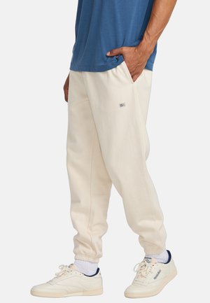 Light beige sweatpants with a ribbed waistband and side pockets, paired with a blue shirt and white sneakers.