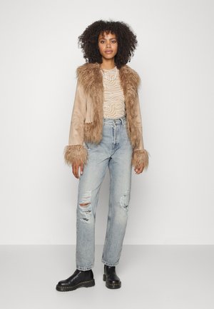 Casaco de pelúcia castanha com mangas texturizadas, blusa com padrão leve, jeans de denim claro e desgastados, e botins pretos.