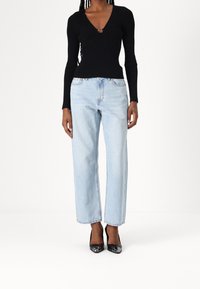 Top negro de manga larga con textura acanalada y un profundo escote en V, combinado con jeans rectos de mezclilla azul claro y tacones altos negros.