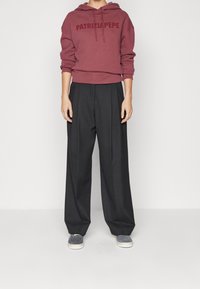 Felpa bordeaux con logo "PATRIZIA PEPE", abbinata a pantaloni neri a gamba larga. Le calzature sono grigie con suole bianche. Insieme semplice e informale.