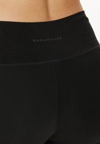 Mustat korkeavyötäröiset legginsit, joissa on sileä pinta, litteät saumat ja "ENDURANCE"-logo huomaamattomalla printillä vyötärölinjassa.