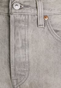 Tessuto di jeans grigio con un primo piano di una vita con un bottone in metallo, cuciture superiori e una tasca laterale con un bordo curvo.