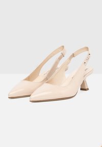 Escarpins à talon bloc en cuir verni beige avec orteils pointus. Présente une sangle réglable avec accents en métal argenté.