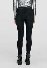 Högmidjade svarta skinny jeans med två bakfickor, med en kroppsnära passform och subtila sömdetaljer. I kombination med svarta snörboots.