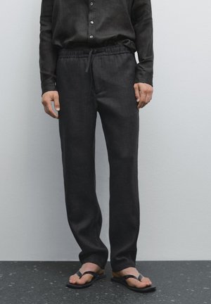 Dark linen pants with an elastic waistband, drawstring detail, and a straight-leg design. Worn with black flip-flops.
