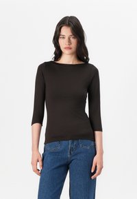 Svart tettsittende topp med båtutringning og trekvartlange ermer, laget av mykt materiale. Kombinert med høytlivs blå jeans.