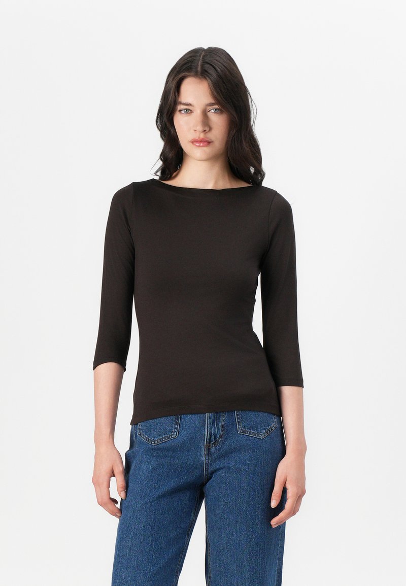 Svart tettsittende topp med båtutringning og trekvartlange ermer, laget av mykt materiale. Kombinert med høytlivs blå jeans.