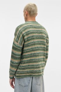 Πλεκτό πουλόβερ με πράσινες και πορτοκαλί οριζόντιες ρίγες, στρογγυλή λαιμόκοψη και άνετη εφαρμογή. Το υλικό φαίνεται μαλακό με υφή.