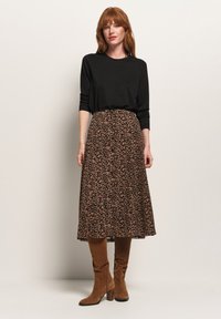 Haut à manches longues noir associé à une jupe mi-mollet marron à imprimé léopard et des bottes marron montant jusqu'aux genoux avec un talon épais.