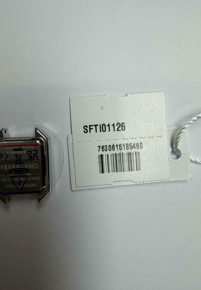 Κάσα ρολογιού Ferragamo από ανοξείδωτο ατσάλι και σημάδια από ζαφειρένιο κρύσταλλο δίπλα σε λευκή ετικέτα τιμής με την ένδειξη SFTI01126 και γραμμικό κώδικα.