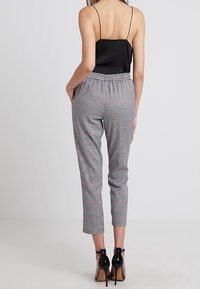 Černý saténový top na tenké ramínka, spárovaný s přiléhavými kostkovanými kalhotami s elastickým páskem. Celkový vzhled doplňují černé vysoké podpatky.