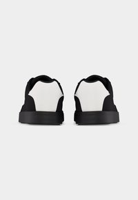 Paire de baskets noires et blanches vues de dos avec semelles noires et empiècement blanc au talon sur un fond uni.