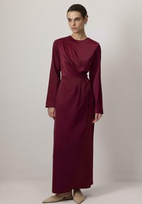 Pikad varrukad, burgundia värvi kleit siledast kangast, millel on drapeeritud eesmine osa ja sobiv vöö. Omab põrandani ulatuvat lõiget ja minimalismi.