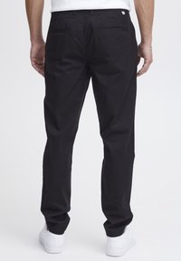 Černé bavlněné kalhoty s volným střihem, vybavené dvěma zadními kapsami a pasem. Kombinovány s bílými teniskami pro kontrast.