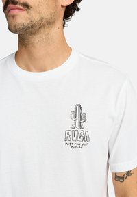 Hvid bomulds t-shirt med en sort kaktus grafik og "RVCA" tekst med "PAST PRESENT FUTURE" nedenfor. Kortærmet og rund hals design.