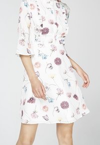 Blommig klänning med korta, utsvängda ärmar; vit bakgrund; pryds av rosa, lila och blå blommor; knälång modell; lättviktsmaterial.