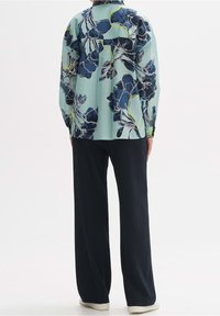 Light blue floral shirt with dark navy flowers, long sleeves, relaxed fit, paired with dark wide-leg pants, displayed against a neutral background.