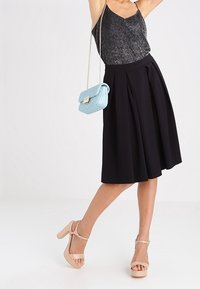 Svart plisserad kjol med en åtsittande midja, matchad med en metallisk ärmlös topp. Tillbehören inkluderar en blå väska och nakna plattformssandaler.