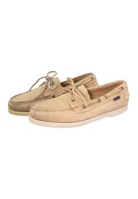 Zapatos náuticos de ante beige con diseño de cordones, ojales de metal y acentos de costura. La suela de goma proporciona tracción.