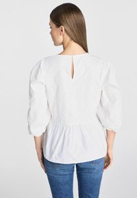 Biała bluzka z marszczonym dołem w kształcie peplum, rękawami 3/4 zakończonymi bufkami oraz detalem w kształcie łezki z tyłu. Wykonana z bawełnianej tkaniny o subtelnej teksturze.