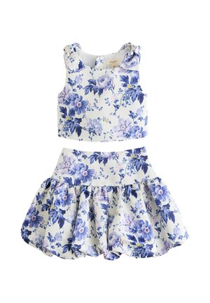 Jong meisje met gevlochten haar, draagt een wit-blauw bloemenmouwloos topje en bijpassende uitlopende rok, lopend op witte sandalen.