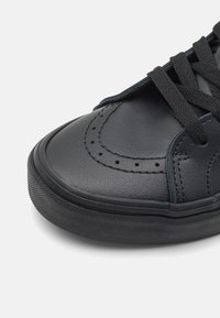 Sneaker in pelle nera con punta arrotondata, finitura testurizzata, dettagli perforati e lacci neri piatti. Suola in gomma con pattern antiscivolo.