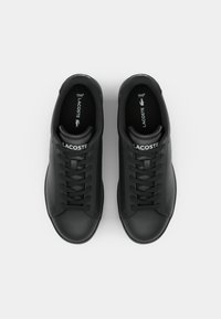 Sorte lædersneakers med en glat overflade, der har en rund tå og flade snørebånd. "LACOSTE" logo på tungen og siden.
