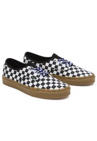 Zapatillas de lona en blanco y negro con diseño de tablero de ajedrez, con cordones azules y suela de goma. Presentan un diseño de perfil bajo y un logo lateral.