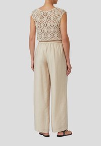 Beige gehaakt top met bloemenpatroon en losse crèmekleurige broek. De broek heeft een elastische tailleband en is gemaakt van lichtgewicht stof.