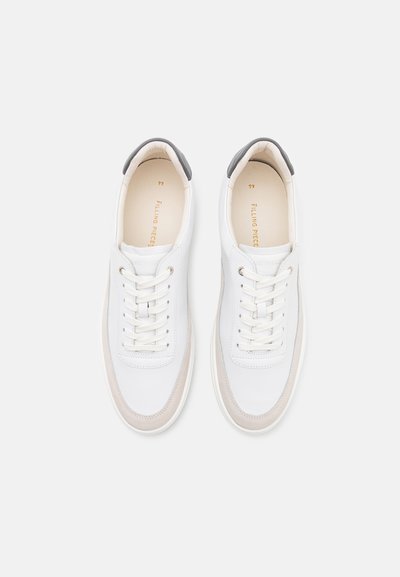 Baskets blanches avec une tige en cuir lisse, des accents en suède beige et un onglet de talon gris. Présente un design à lacets et un logo en relief.
