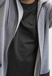 Felpa con zip grigia con maglia interna nera a rete, caratterizzata da tessuto liscio, coulisse regolabili e vestibilità comoda.