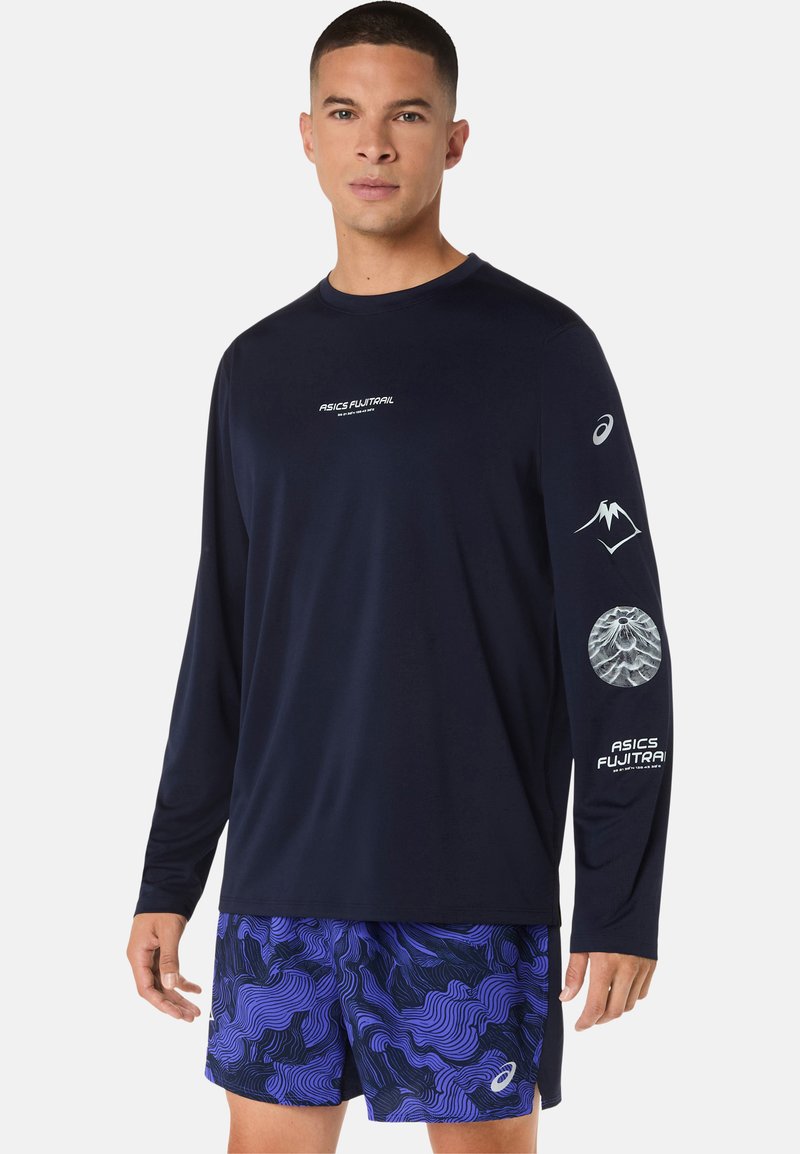 Haut de sport à manches longues bleu marine avec logos blancs et motifs de montagnes sur les manches, associé à un short violet à motifs. Adapté pour le sport.