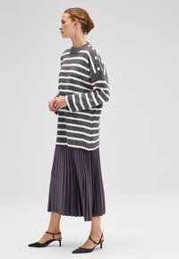 Sweter w paski w odcieniach szaro-białych, teksturowany, z guzikami na ramieniu; połączony z plisowaną szaro-sukienką i czarnymi butami na obcasie.