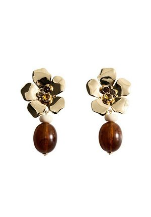 Cercei aurii în formă de floare, cu pietre prețioase mici în centru și o mărgea ovală mare maro atârnând sub fiecare floare.