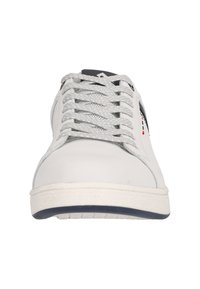 White sneaker with a smooth leather upper, textured gray laces, padded tongue, and navy rubber sole featuring a minimalistic design and logo accents.