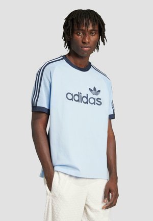 Világoskék Adidas póló, sötétkék részletekkel, elöl logóval, hálós betétekkel a vállakon és rövid ujjakkal.