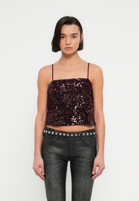 Haut court bordeaux à sequins avec fines bretelles, associé à un pantalon noir aspect cuir avec une ceinture cloutée. Surface texturée et brillante.