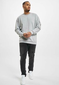 Grauer Sweatshirt mit geripptem Kragen und Bündchen, kombiniert mit abgenutzten schwarzen Jeans und weißen Sneakers, ausgestattet mit einer Tasche mit Reißverschlussdetail.