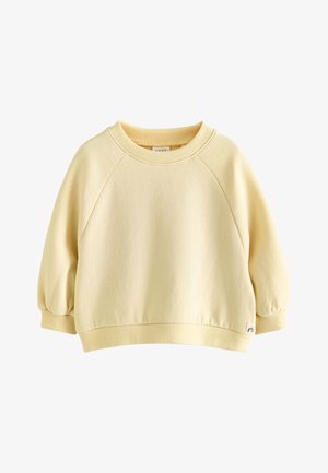 Krém sárga hosszú ujjú kisgyermek pulóver bordázott mandzsettákkal, szegéllyel és nyakrésszel, az alján egy kis szivárványos címkével.