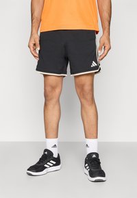 Black athletic shorts with a textured mesh design, accented by a white trim. Paired with black shoes and white socks featuring a logo.