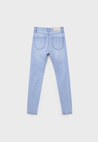 Jean skinny en denim bleu clair vu de dos avec deux poches arrière et un patch de marque beige sur la ceinture.